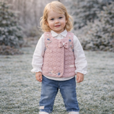 Child wearing a pink quilted vest with floral patterns outdoors on a frosty day.