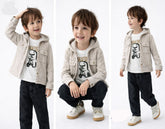 Three poses of a child wearing a beige jacket, white t-shirt with a graphic, and black pants on a white background.